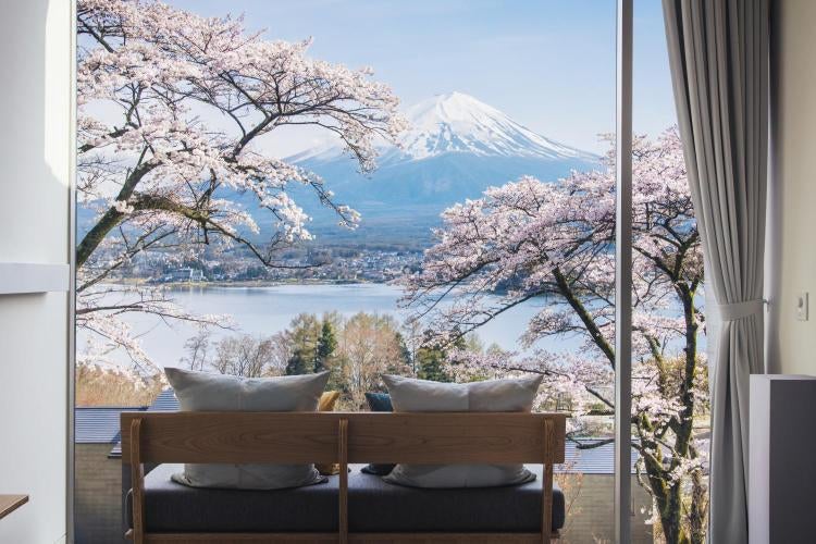 Modern luxury cabin with floor-to-ceiling windows perched on Mount Fuji hillside, overlooking Lake Kawaguchi and misty forest views