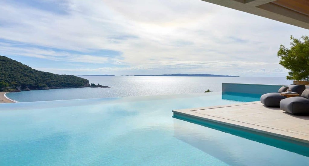 Luxurious seaside hotel with white minimalist architecture, infinity pool overlooking azure Ionian Sea, and sleek modern design in scenic Greek coastal landscape