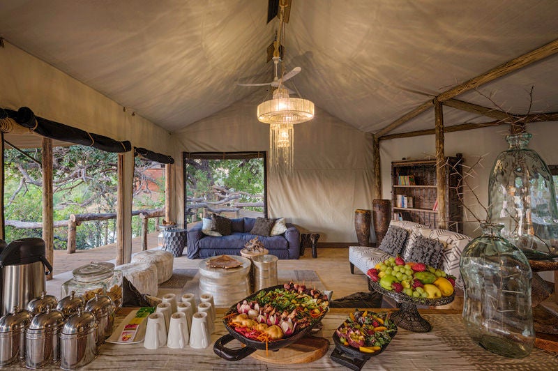 Elevated safari tent lodge with private wooden deck overlooking lush green Okavango Delta wetlands at sunset, luxury outdoor seating