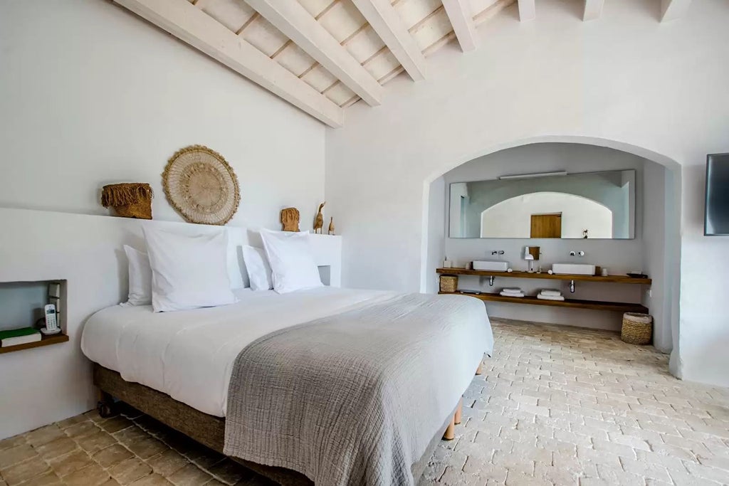 Elegant Spanish suite with panoramic coastal view, wooden floors, minimalist design, white linens, and warm sunset lighting through floor-to-ceiling windows