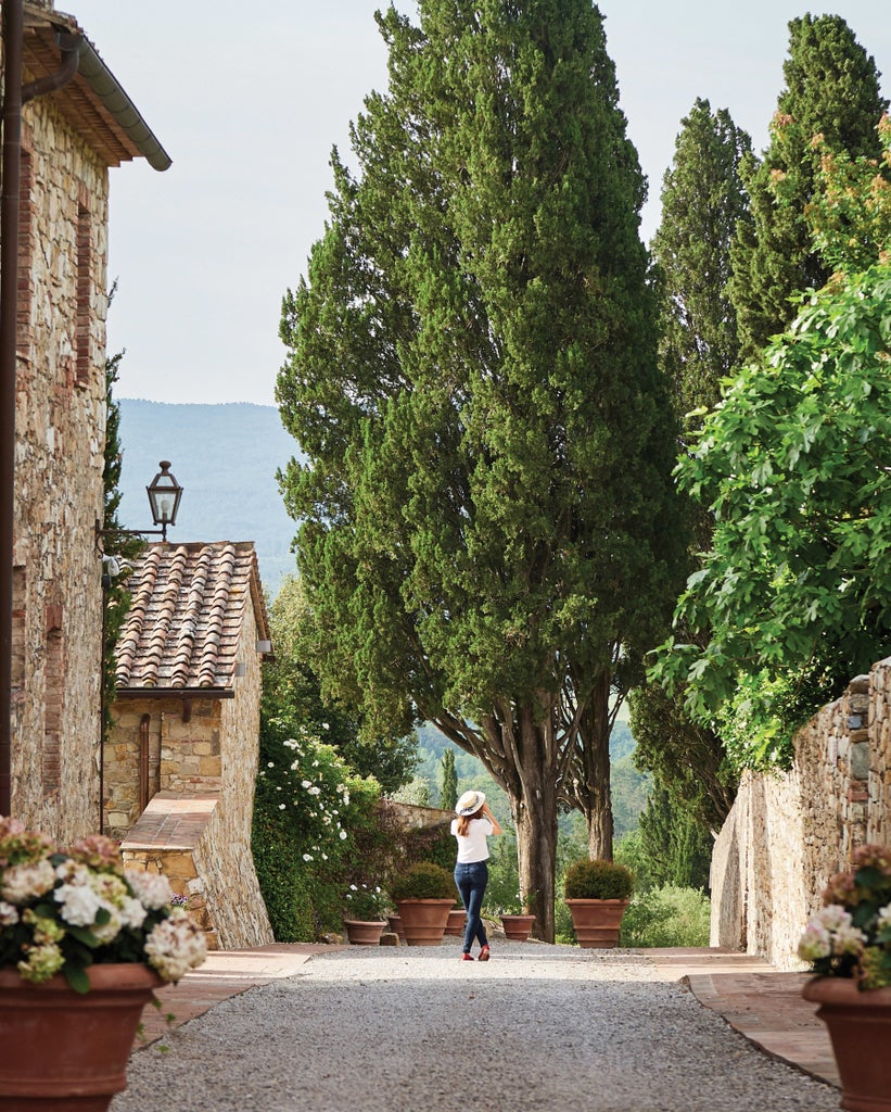 Historic Italian castle hotel with stone facade and cypress trees, set against rolling Tuscan hills at golden sunset hour