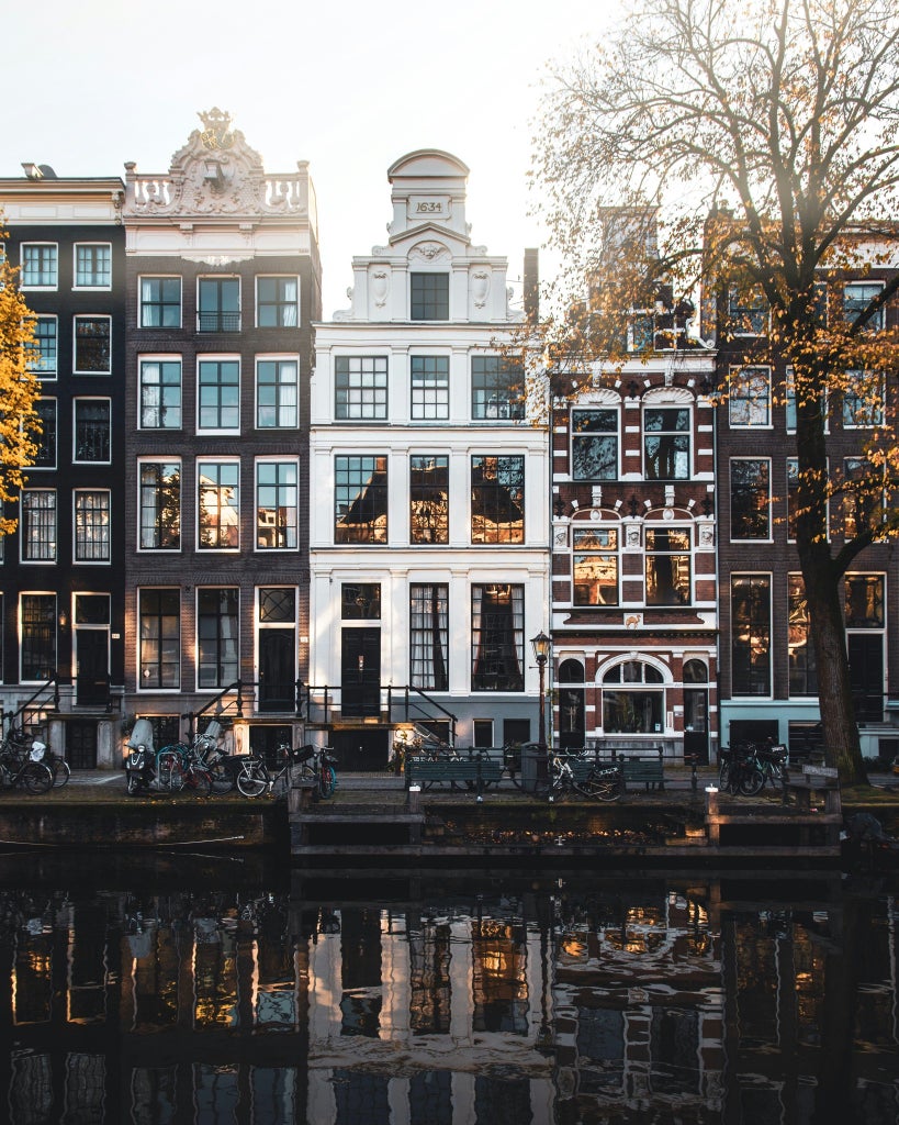 Historic canal houses with elegant facades line Amsterdam's waterway at dusk, golden lights reflecting on calm water beneath cloudy skies