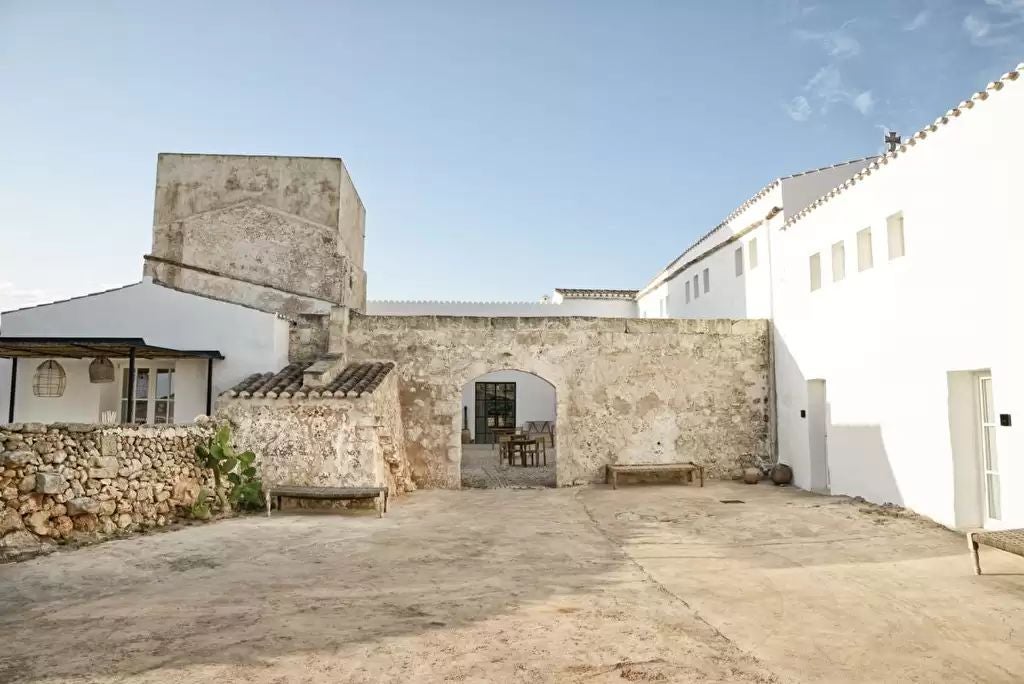 Luxurious stone tower hotel in scenic Spanish coastal landscape, featuring stone walls, Mediterranean cypress trees, and elegant architectural details