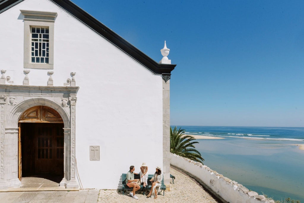 Elegant Portuguese countryside retreat with rustic wooden veranda, lush green landscape, traditional stonework, and warm golden sunlight filtering through trees