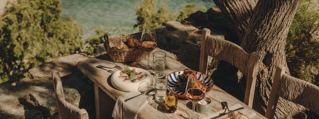 Luxurious whitewashed Greek hotel with minimalist design, overlooking azure Aegean waters and rocky coastal landscape at sunset