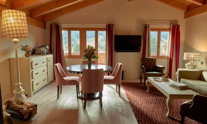 Luxurious chalet-style suite with panoramic mountain views, elegant wooden furnishings, plush king bed, and Swiss alpine landscape through large windows