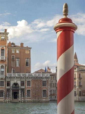 Elegant Venetian palazzo on Grand Canal, with ornate gothic windows, rich burgundy facade, and gleaming canal waters reflecting historic architecture at dusk.