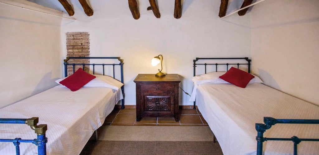 Rustic Spanish countryside hotel room with elegant white linens, wooden beams, and warm terracotta tiles at Cortijo del Marqués estate