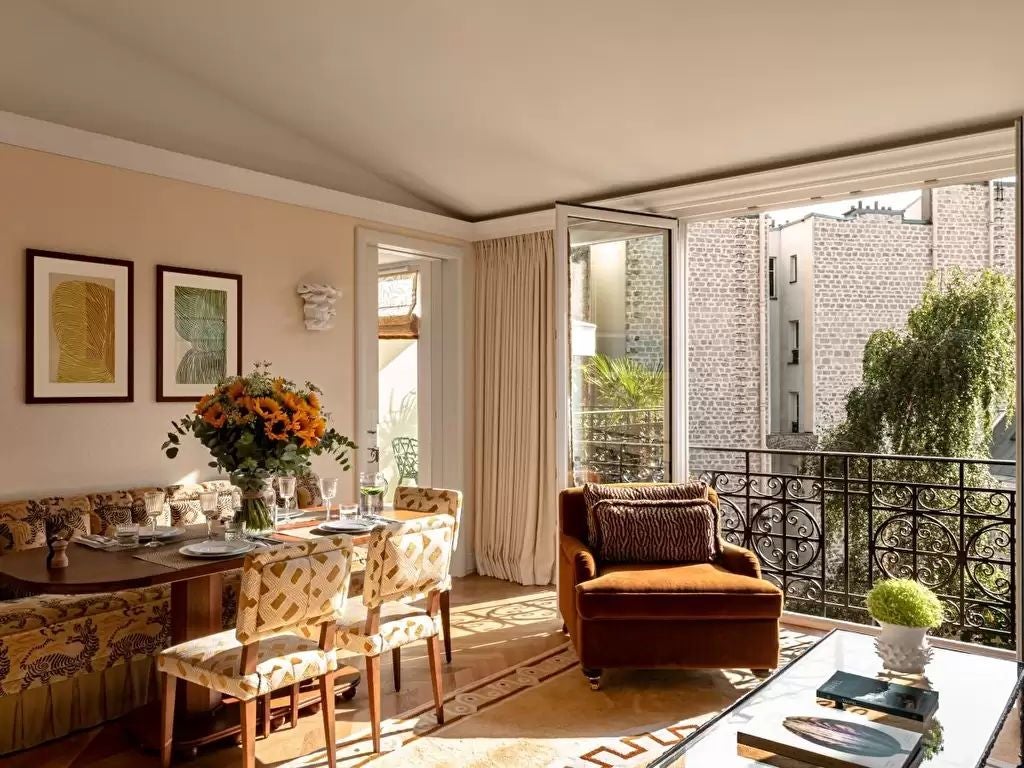 Opulent Parisian apartment suite with crystal chandelier, antique furnishings, decorative fireplace, and floor-to-ceiling windows with drapes