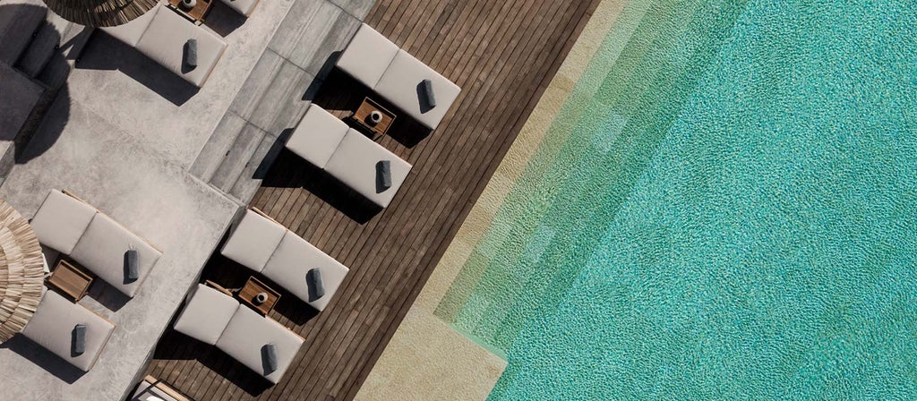 Contemporary luxury hotel exterior with white minimalist architecture, infinity pool overlooking Mediterranean Sea, and elegant poolside loungers