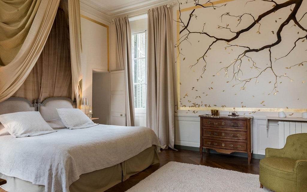 Elegant French hotel room with soft rose-colored walls, antique wooden furniture, and delicate floral curtains overlooking lush gardens at Château Hôtel de Saint Paterne