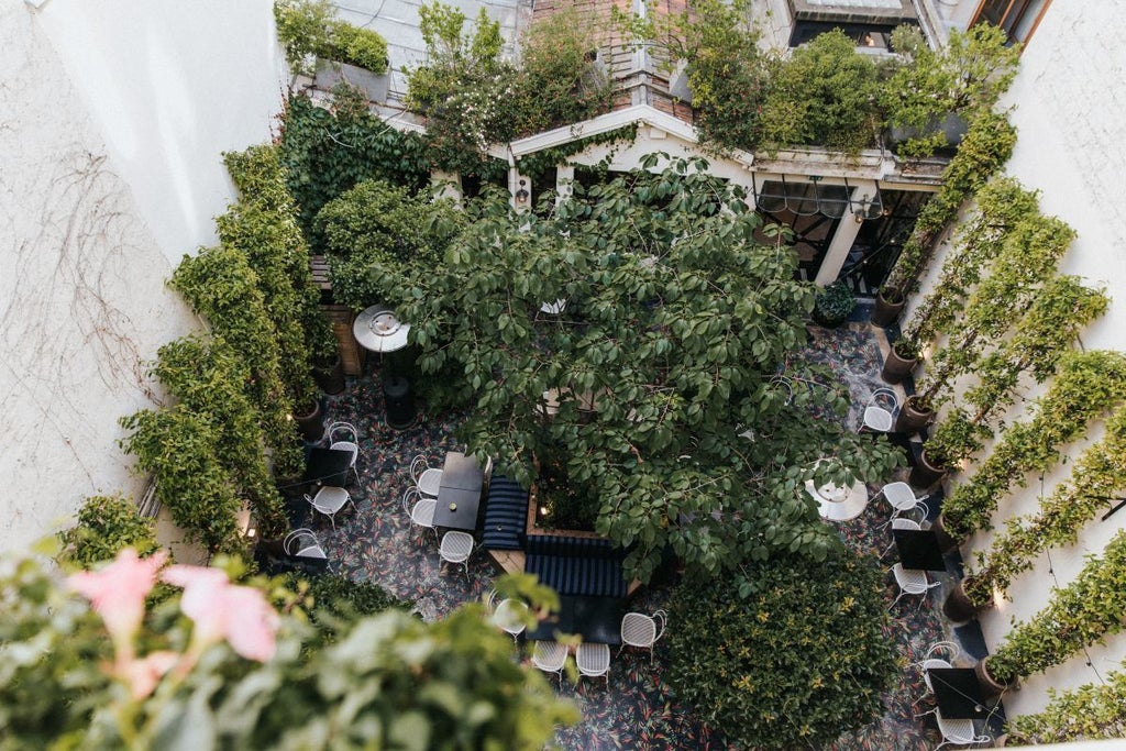 Elegant Parisian boutique hotel with soft pastel facade, ornate wrought-iron balconies, and charming window boxes filled with blooming flowers