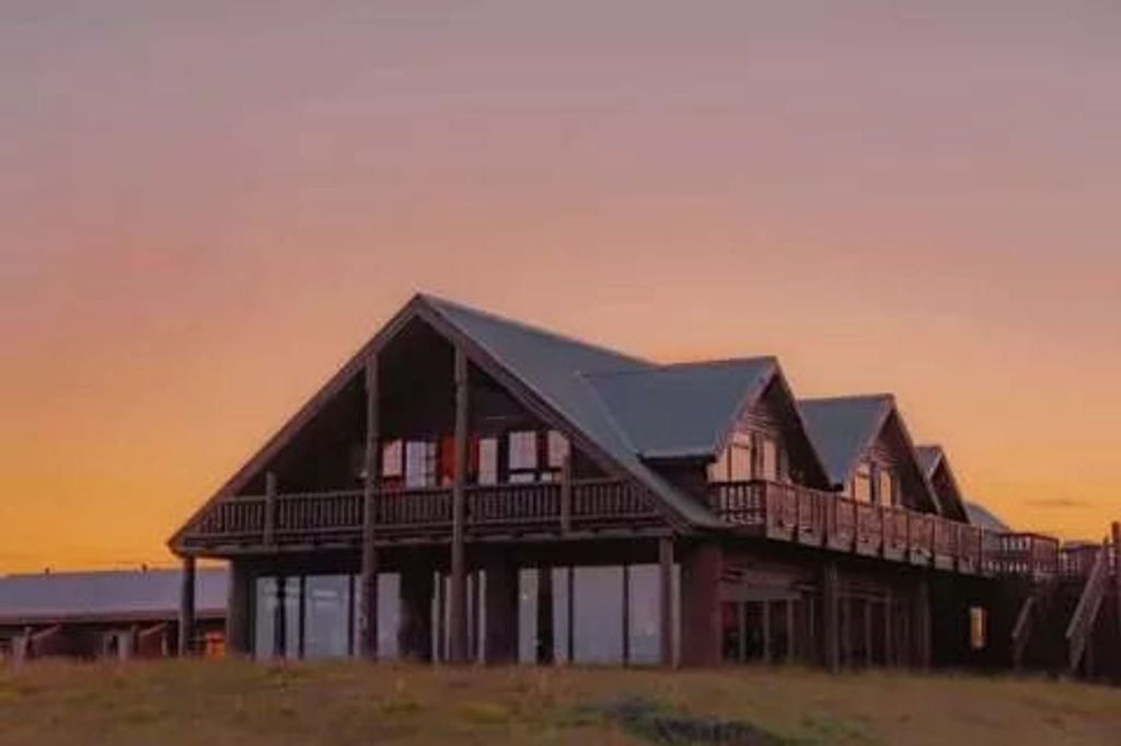 Luxury Hotel Rangá's wooden facade nestled in snowy Icelandic landscape, illuminated by warm lights with mountains in background