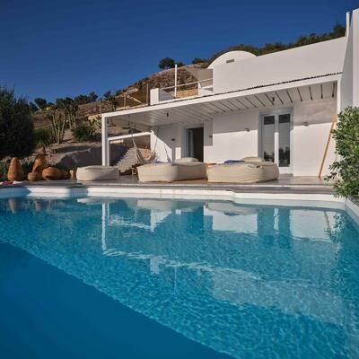 Elegant white-washed Santorini suite with minimalist design, featuring private balcony overlooking azure Aegean Sea and traditional Cycladic architectural details