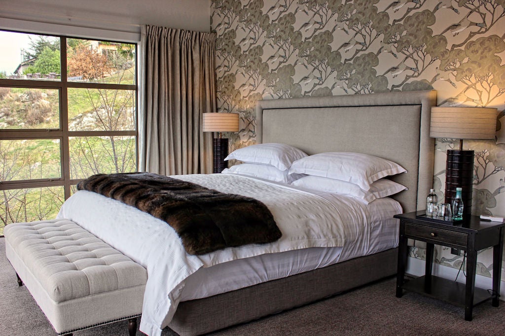 Luxury lakefront suite featuring elegant white furnishings, king bed with mountain views, and opulent marble bathroom in Queenstown