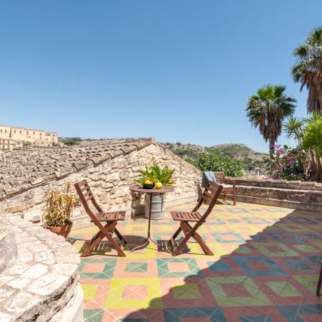 Elegant rustic Italian hotel room with stone walls, handcrafted wooden furniture, soft linen bedding, and warm terracotta floor tiles in Sicilian style