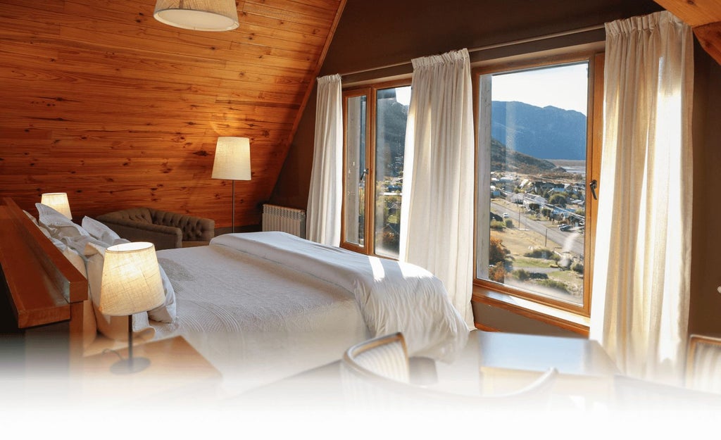 Elegant premium hotel room with plush white bedding, modern wooden furnishings, and large windows overlooking scenic Argentine landscape at Los Cerros Boutique Hotel