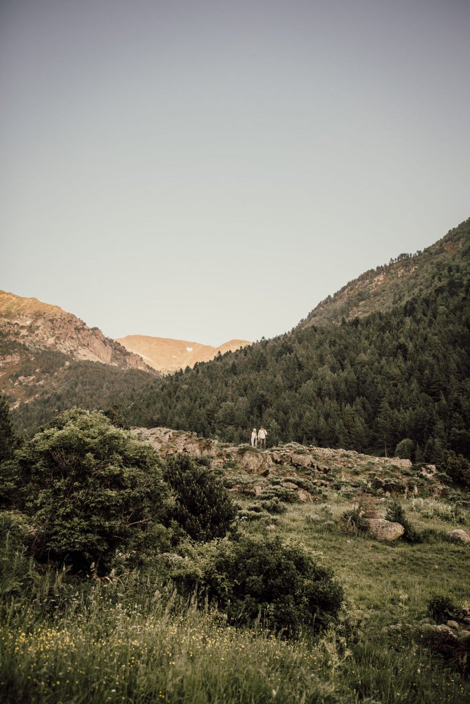 Luxurious mountain lodge nestled in Andorran alpine landscape, featuring rustic stone exterior, wooden balconies, and snow-capped peaks in background.