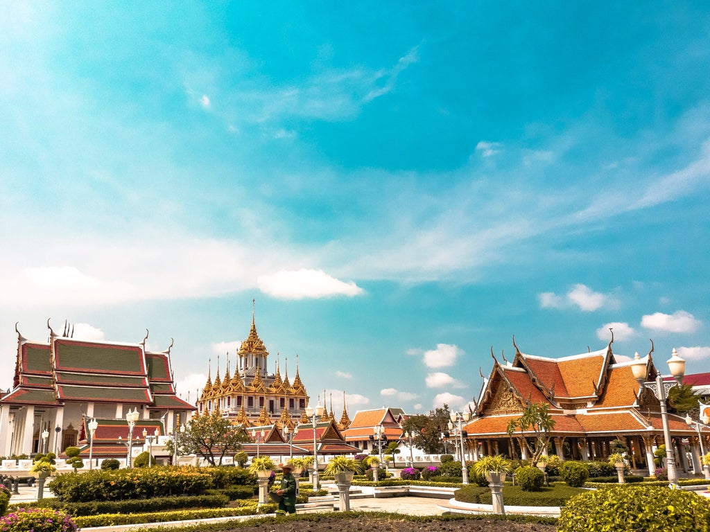 Opulent golden Buddha statue gleaming in sunlight, ornate temple architecture, vibrant Thai silk, and shimmering Bangkok cityscape backdrop