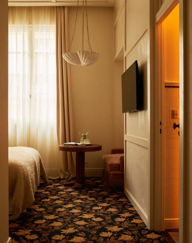 Elegant junior suite at Château Voltaire with plush white bedding, ornate gold-framed mirror, and soft natural lighting in a chic Parisian style