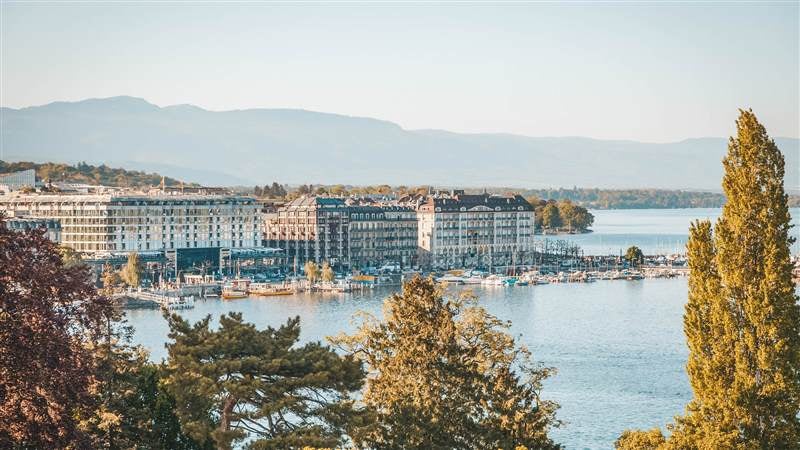 Elegant five-star Swiss hotel with ornate Belle Époque facade, grand entrance, and iconic flags overlooking Lake Geneva at sunset