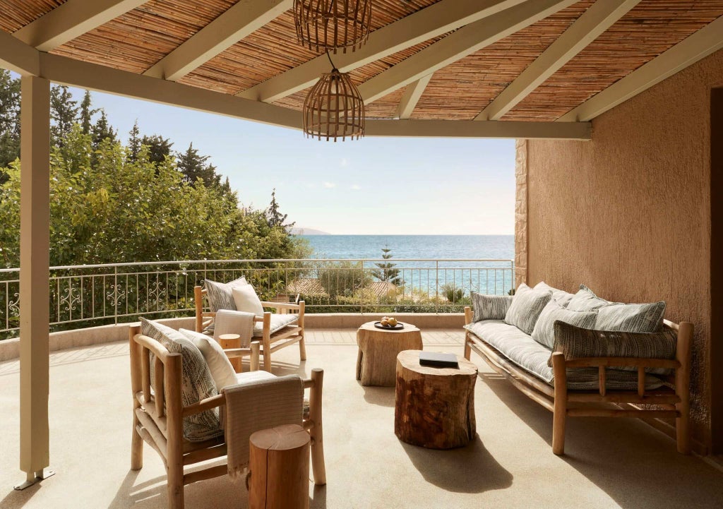 Luxurious boutique hotel terrace overlooking azure Ionian Sea, with infinity pool, minimalist white furniture, and lush Mediterranean landscape at sunset