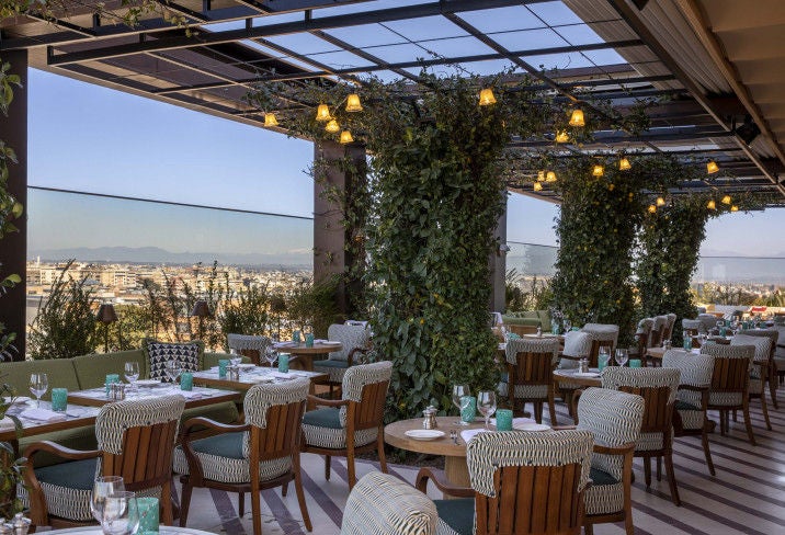 Elegant rooftop terrace at SoHo House Rome with striped umbrellas, plush loungers and panoramic views over historic Roman skyline at sunset