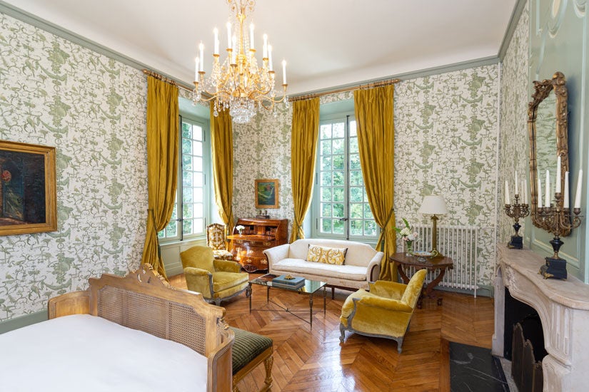 Elegant corner king room with ornate crown molding, crystal chandelier, antique furnishings and panoramic French countryside views