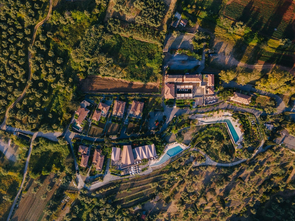 Historic stone-built luxury hotel nestled on Greek hillside with infinity pool overlooking Mediterranean Sea and traditional architecture