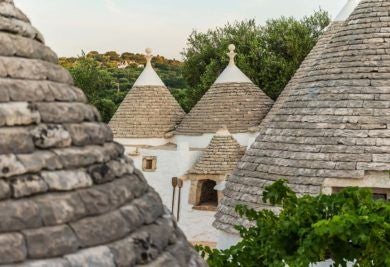 Rustic stone trulli houses in Puglia, Italy, with whitewashed walls and conical roofs, set against a warm golden sunset landscape