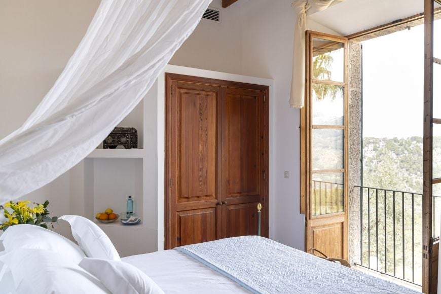 Elegant stone-walled bedroom with plush white bedding, rustic wooden furnishings, and soft natural light in a luxurious Spanish countryside retreat.