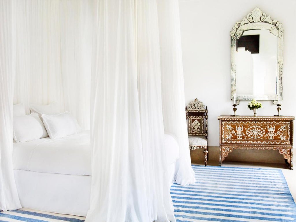 Elegant Moroccan riad with ornate archways, traditional courtyard fountain, white pillars and lush palm trees under bright blue sky