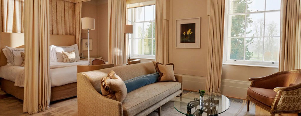 Elegant Mansion House Junior Suite at Coworth Park, showcasing plush cream furnishings, sophisticated decor, and soft natural lighting from large windows