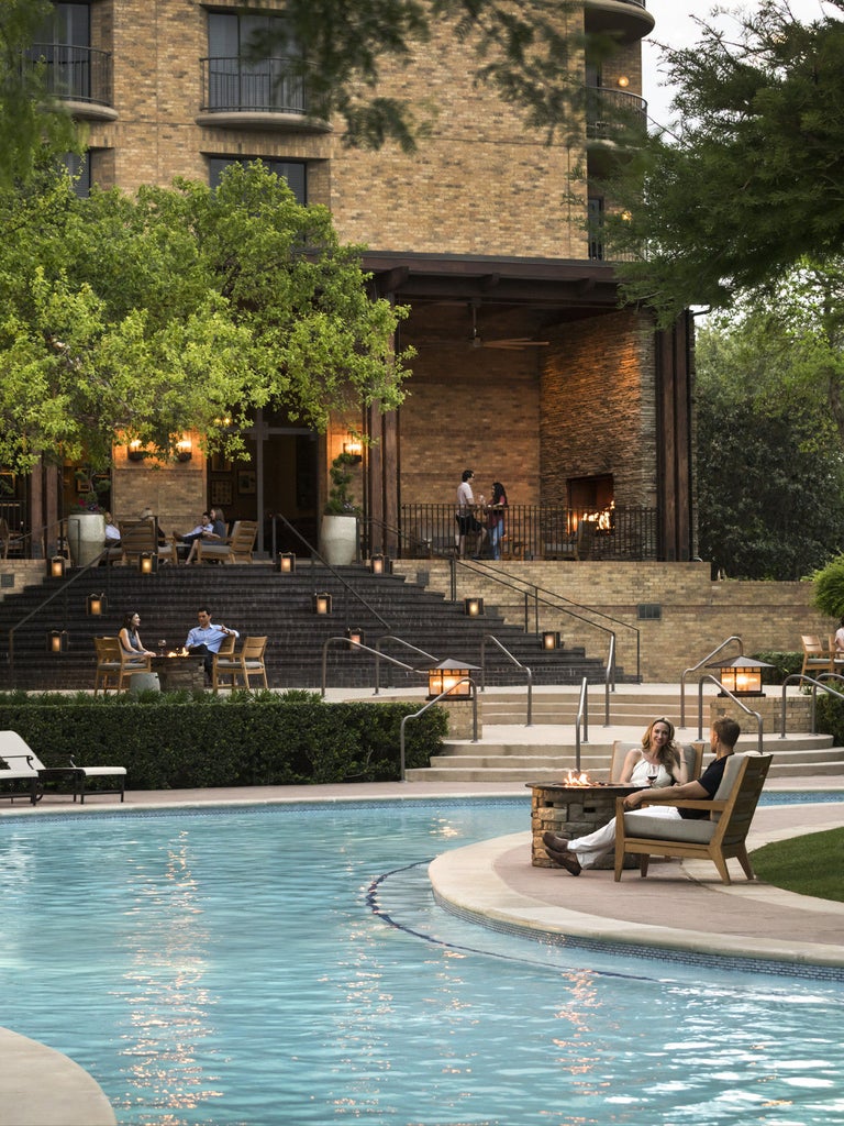 Modern luxury high-rise hotel with glass facade reflecting sunset sky, surrounded by manicured gardens and palm trees in Dallas cityscape