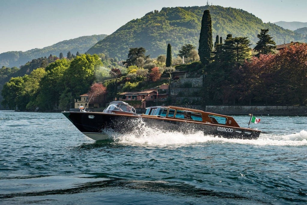 Elegant wooden boat cruising Lake Como's turquoise waters, passing historic Italian villas with snow-capped Alps in the distance