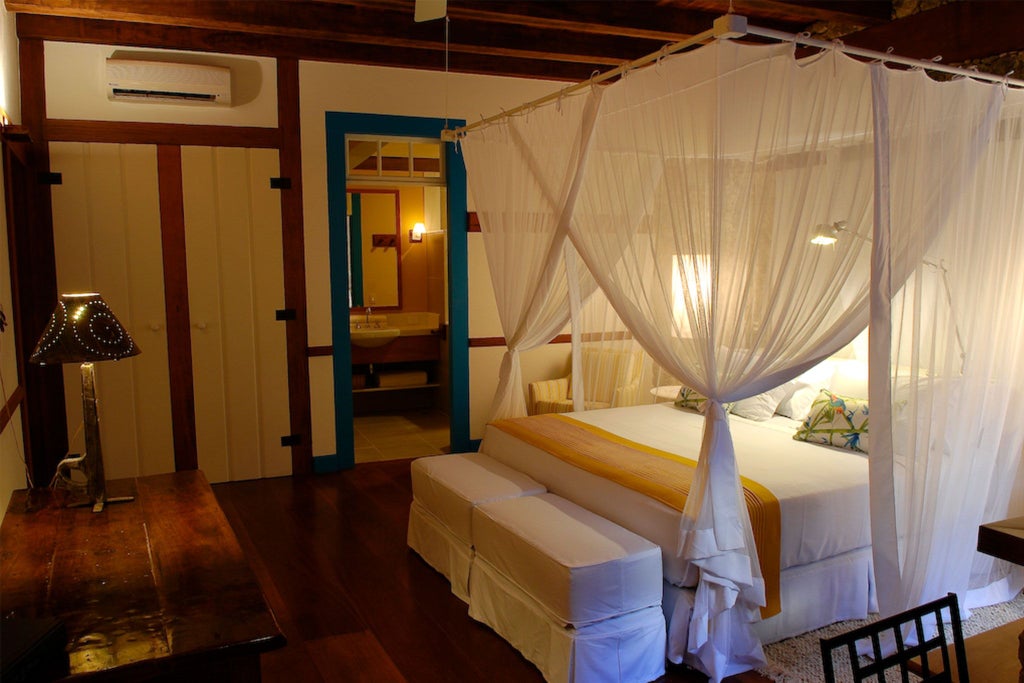 Elegant yellow-themed hotel suite with colonial Brazilian architecture, white linens, turquoise accent walls, and graceful wooden furniture in boutique resort setting