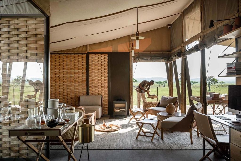 Elegant safari tent with private wooden deck overlooking vast African savanna at sunset, featuring plush outdoor lounge furnishings