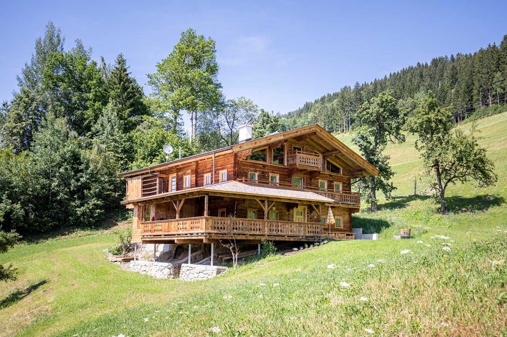 Traditional alpine hotel with wooden balconies and terraces nestled in snow-capped mountains, surrounded by evergreen forest at sunset