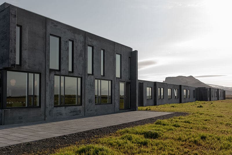 Luxurious minimalist hotel in Iceland with black wooden exterior, floor-to-ceiling windows reflecting snow-covered mountain landscape