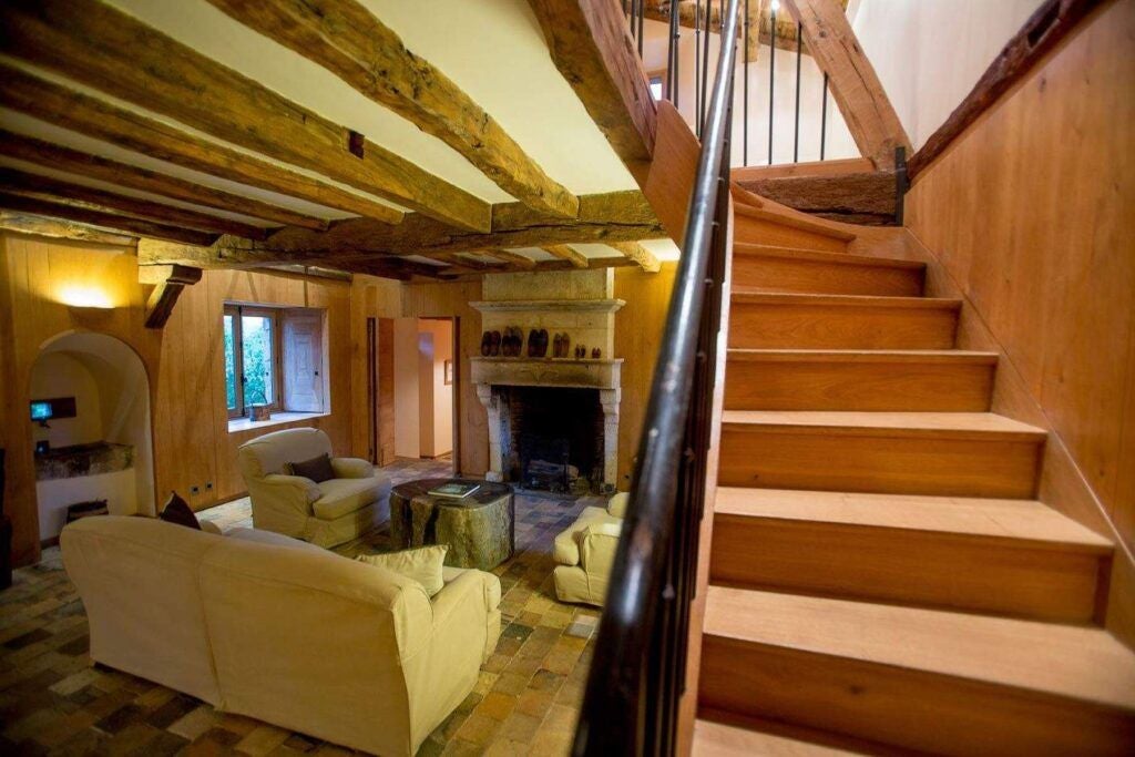 Luxurious rustic cottage bedroom with stone walls, elegant wooden furnishings, soft neutral tones, and large windows overlooking French countryside landscape