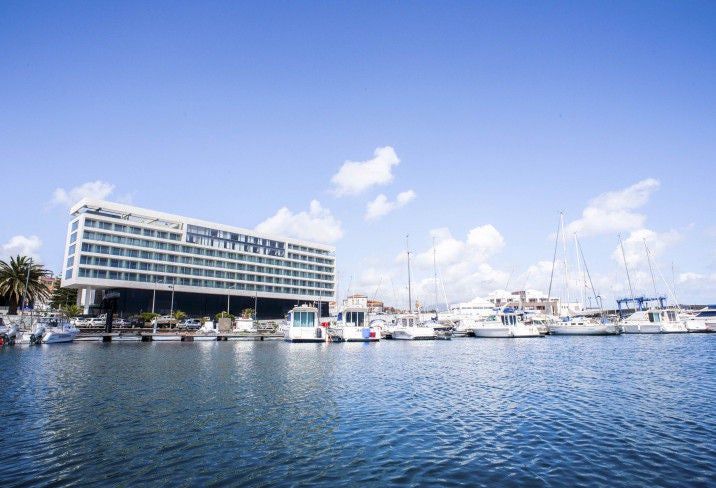 Modern luxury hotel exterior featuring glass facade, clean lines, and rooftop infinity pool overlooking Ponta Delgada's harbor at sunset