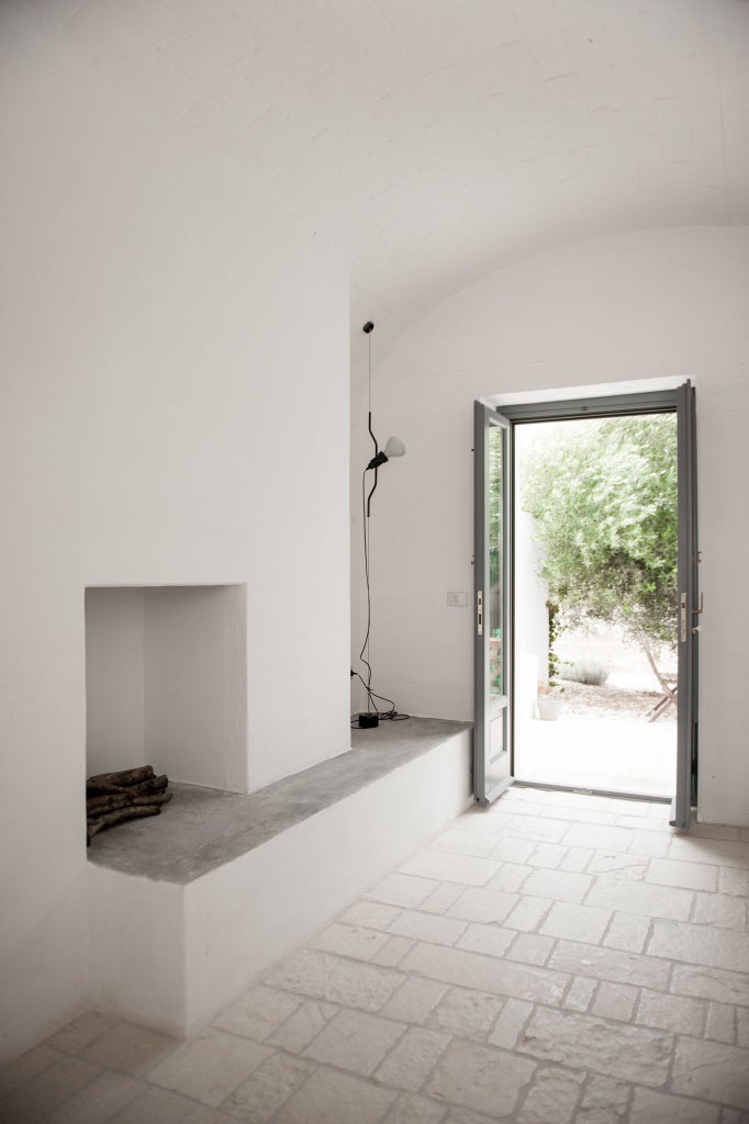 Minimalist white bedroom with arched window, crisp linens, terracotta floor tiles, overlooking Italian countryside near Ostuni, Puglia