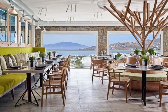 Luxurious white-washed Cycladic hotel with infinity pool overlooking azure Aegean Sea, showcasing elegant minimalist architecture against Mykonos landscape