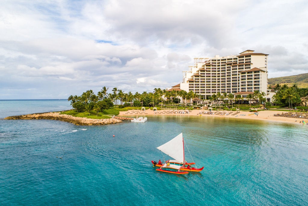 Oceanfront luxury resort in Ko Olina with infinity pools cascading towards pristine beach, surrounded by swaying palm trees at sunset