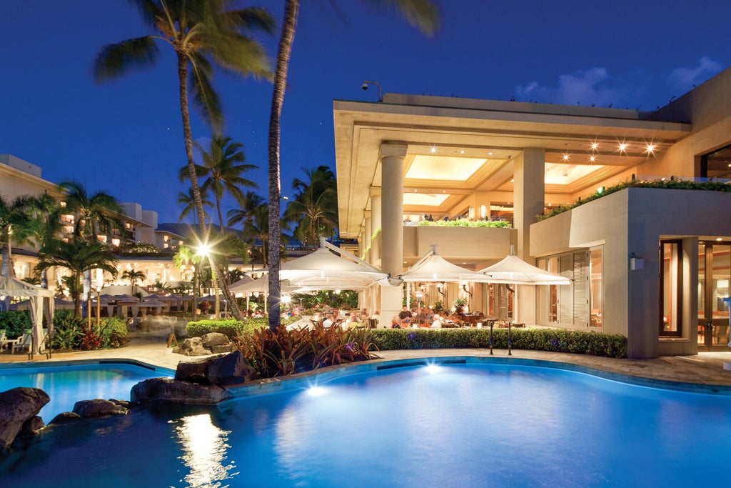 Oceanfront hotel with infinity pools overlooking a pristine beach, surrounded by palm trees and luxury cabanas at sunset in Maui