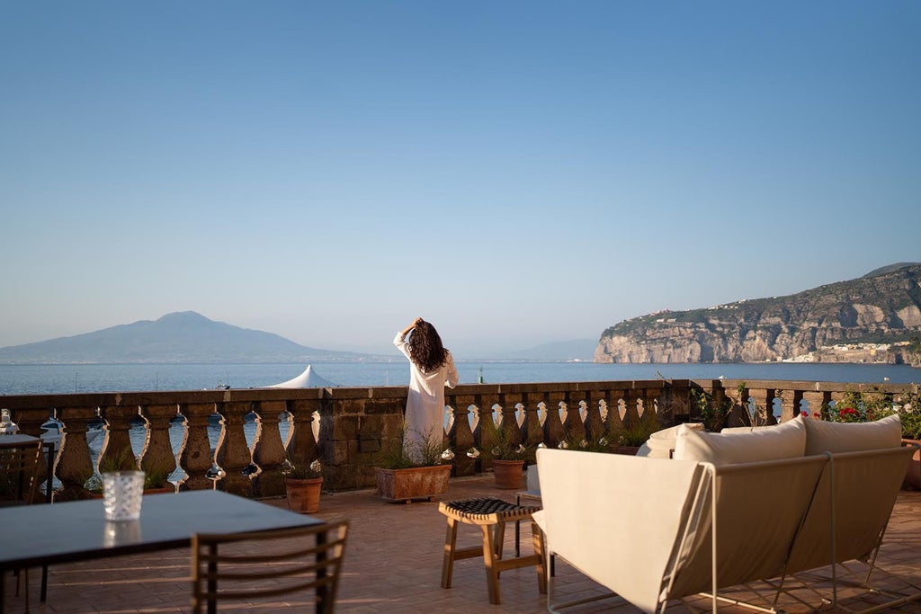 A luxurious seaside hotel with stone balconies and white shutters overlooking the crystal-clear Mediterranean waters in Sorrento, Italy