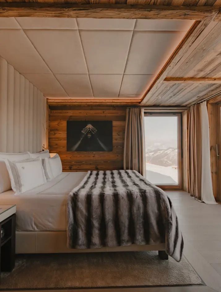 Luxurious alpine bedroom in Ultima Hotel Courchevel, featuring elegant white decor, plush bedding, and panoramic mountain views through large windows.