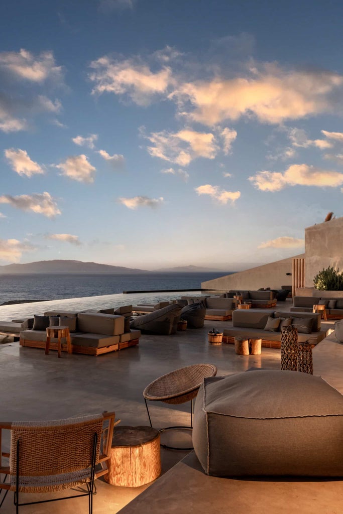 Luxury cave-style suite with private infinity pool overlooking Santorini's caldera at sunset, featuring whitewashed walls and minimal decor