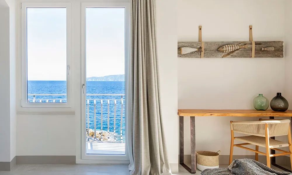 Luxurious junior suite with elegant white interior, direct beach access, plush king bed, and panoramic sea view in coastal Italian resort setting