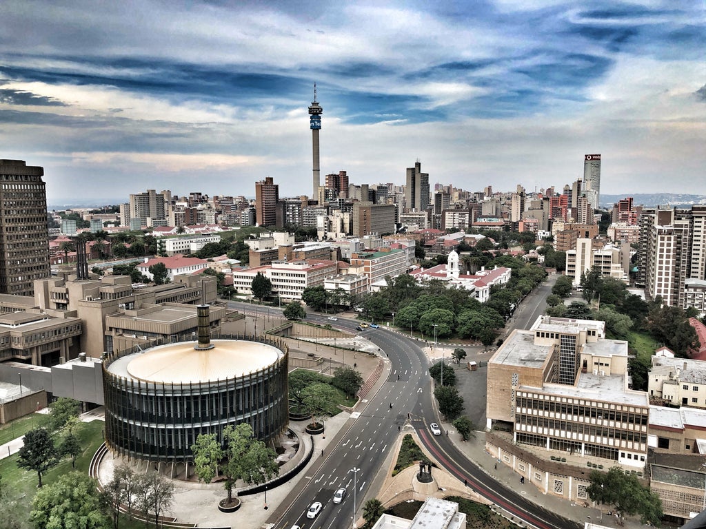 Panoramic view of Johannesburg skyline at sunset with modern skyscrapers, glowing city lights and iconic Hillbrow Tower rising above CBD